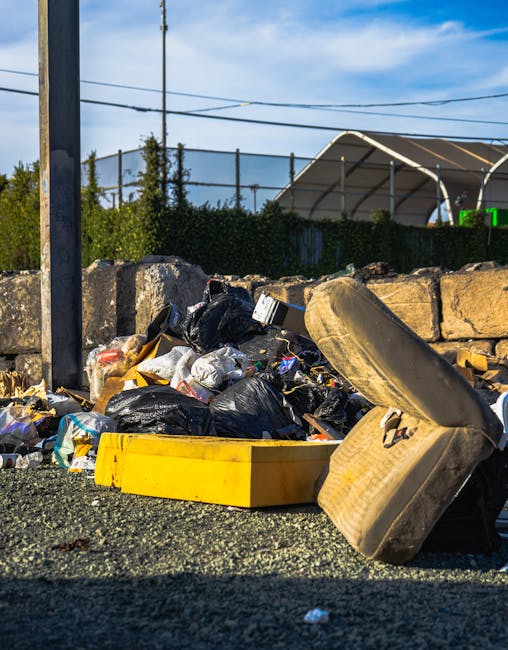 Multiple large transparent plastic bags filled with assorted waste and discarded items, placed on the pavement outside a commercial establishment in an urban environment. The bags contain various mate